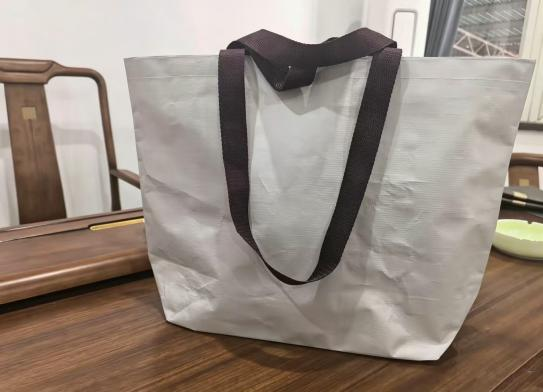 Gray hotel tote bag with contrasting wraparound handle webbing extending under the base.